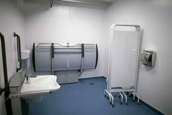 disabled toilets with a toilet and handrails, a sink mounted to the wall with handrails and a stretcher against the wall