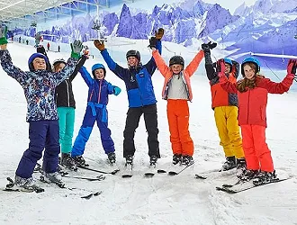 Group of children on skis wearing brightly coloured ski gear cheering with their instructor
