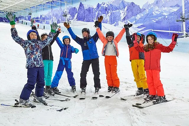 Group of children on skis wearing brightly coloured ski gear cheering with their instructor