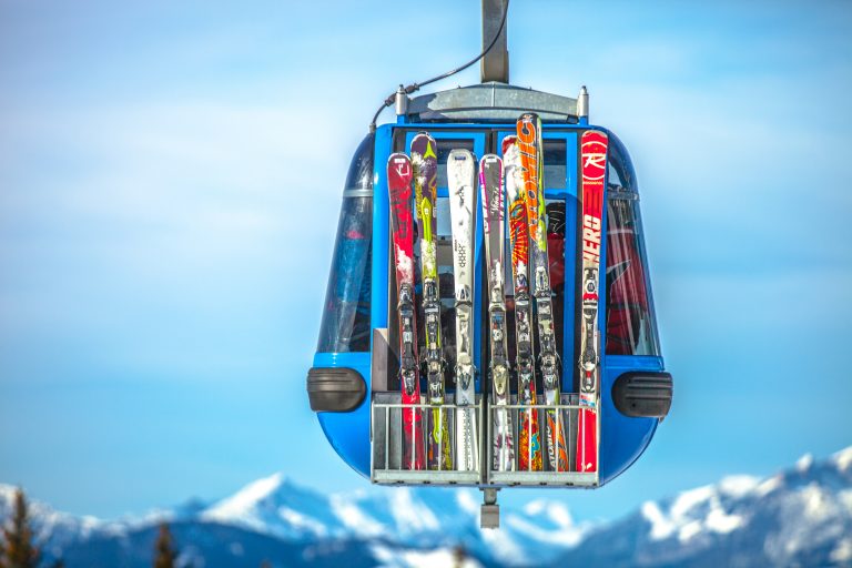 a blue cable car suspended in the air with a bunch of skis attached to the back of it