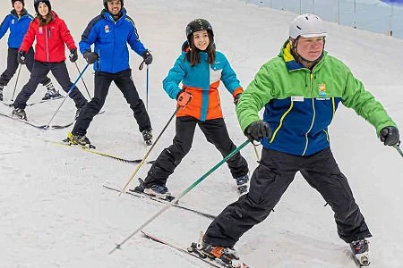 Group of adults on skis following their instructor snow ploughing