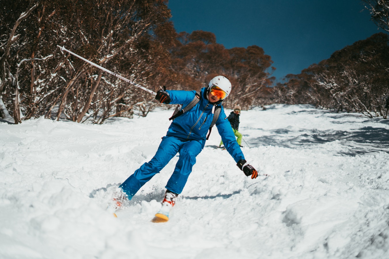A person wearing all blue snow clothing, skiing down a steep snowy slope with trees either side